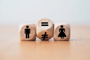 Wooden blocks show a man icon, an equals/not-equals pair in the center, and a woman icon—conveying gender equality and inequality.