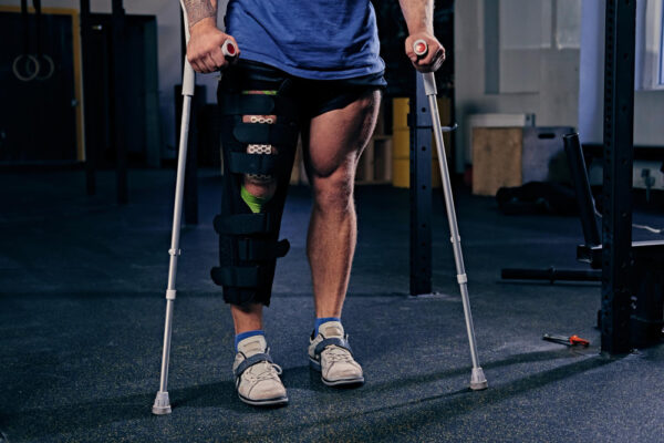 Person wearing a knee brace on the left leg and using forearm crutches in a gym setting